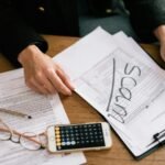 Hands of a person examining tax forms labeled as scam with calculator and papers.
