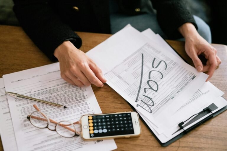 Hands of a person examining tax forms labeled as scam with calculator and papers.