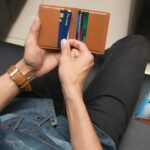 A close-up of a man holding a wallet containing credit cards and an ID inside a room.